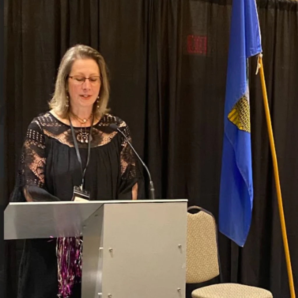 Angela Aalbers Reeve is the speaker stands at a podium at the MVAN Women in Business Awards, with an Alberta flag beside the stage.