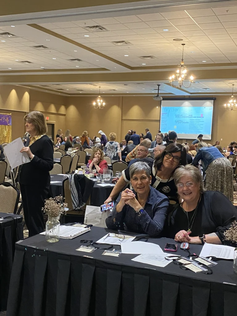 Event organizers seated at a table in a busy ballroom during the MVAN Women in Business Awards luncheon with attendees networking in the background