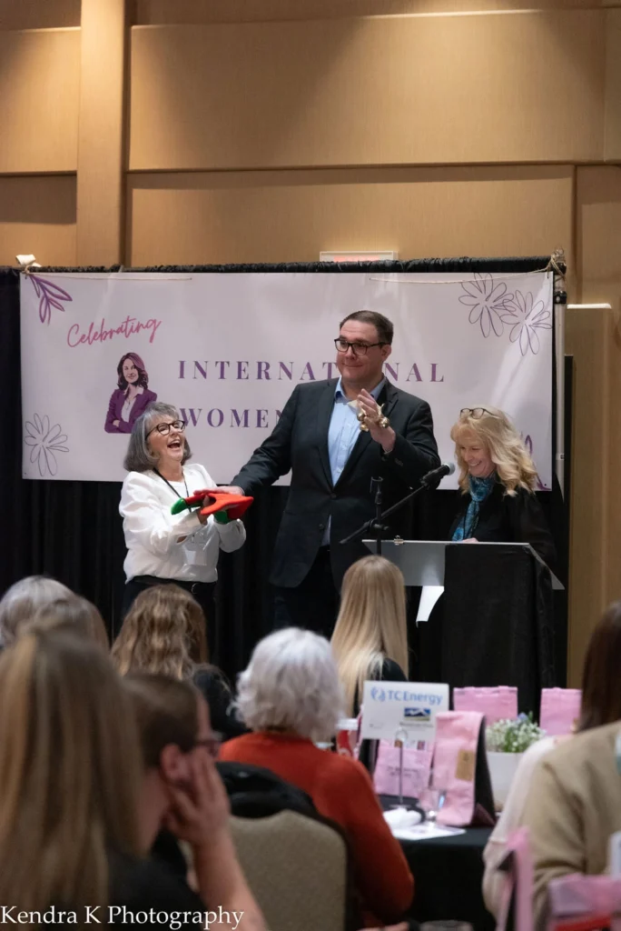 Speaker and presenters on stage in front of an International Women’s Day banner at the 2025 MVAN Women in Business Awards luncheon