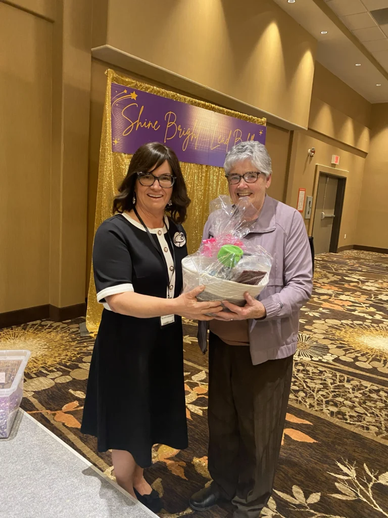 Two women holding a wrapped gift basket with a purple bow during an appreciation presentation at the MVAN Women in Business Awards