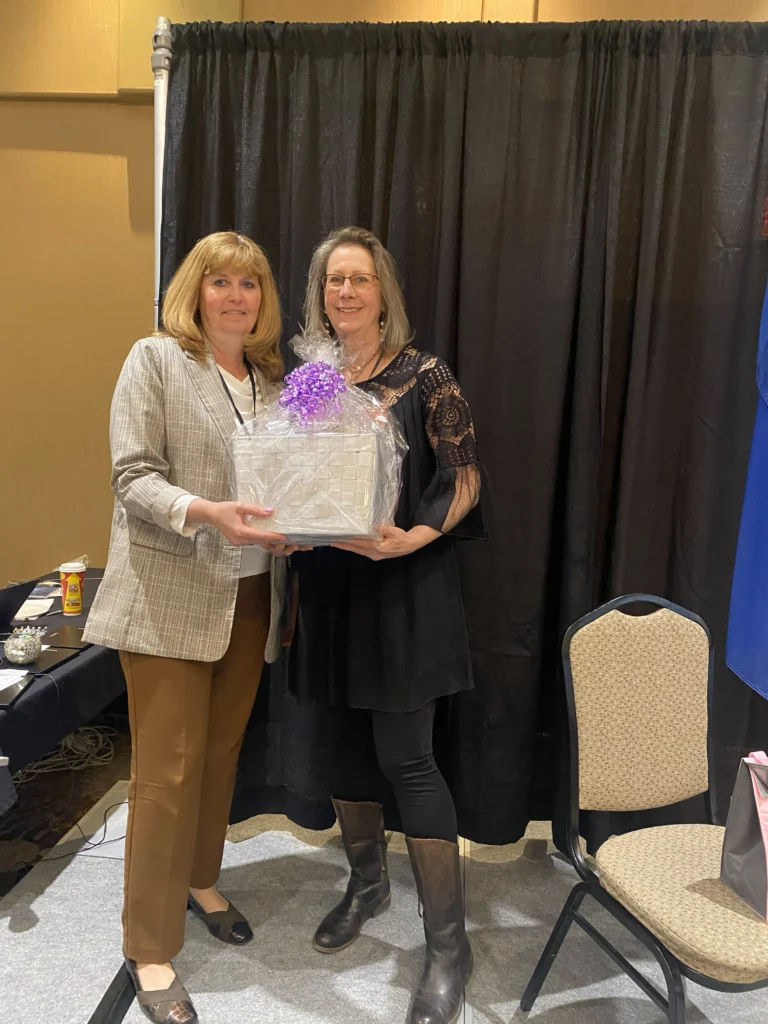 Two women posing with a wrapped gift basket during the 2025 MVAN Women in Business Awards event