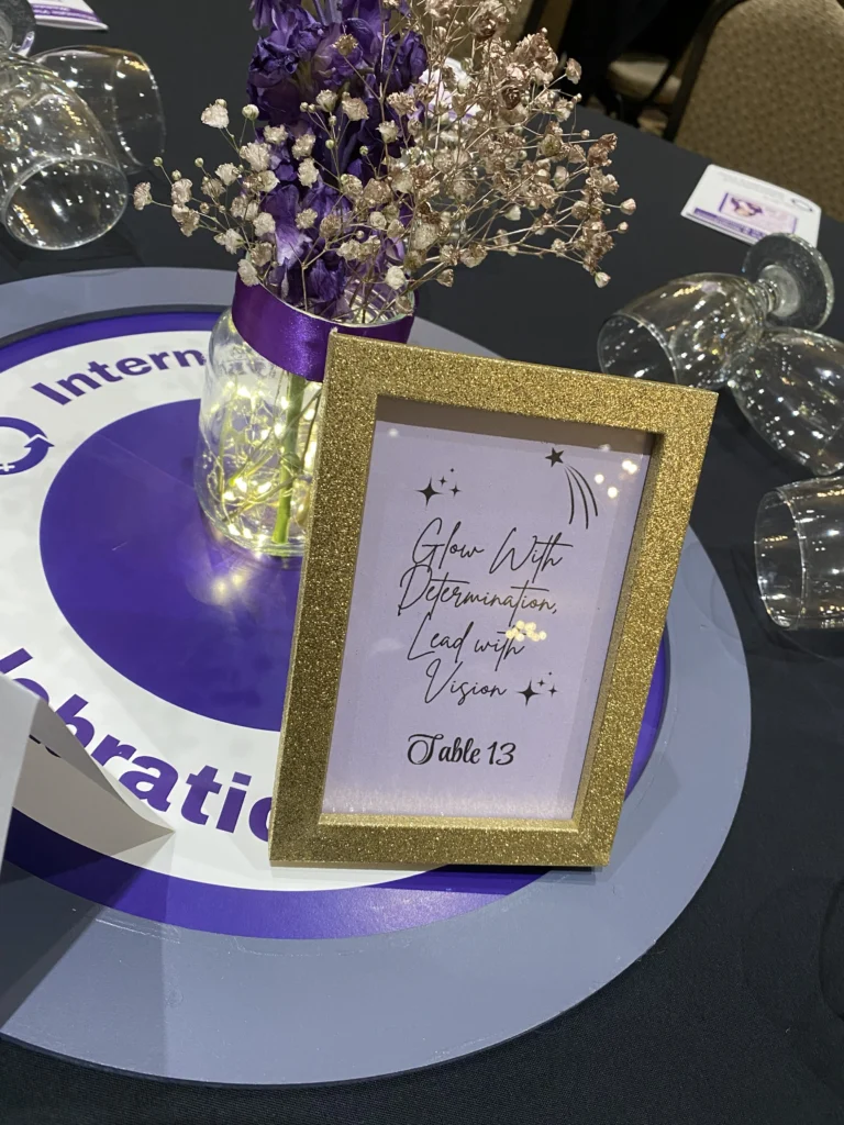 Table décor with purple flowers and a gold-framed sign reading “Glow With Determination, Lead with Vision” at the MVAN Women in Business Awards